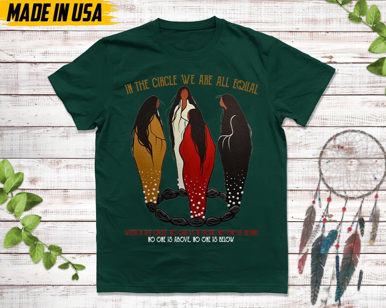 Puede incluir: Camiseta verde oscuro con el texto "IN THE CIRCLE WE ARE ALL EQUAL". La camiseta presenta una ilustraci&oacute;n de tres figuras con vestidos largos, con el texto "WHEN OF THE CIRCLE, NO ONE IS ABOVE, NO ONE IS BELOW". Las palabras "MADE IN USA" est&aacute;n en la parte superior.