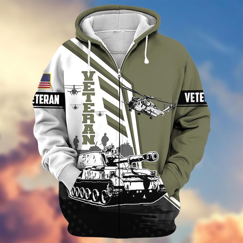 Pode incluir: Um casaco com capuz e z&iacute;per com tema militar. O design apresenta um tanque, helic&oacute;pteros e a palavra "VETERAN" em branco. A manga esquerda tem uma bandeira americana. O esquema de cores inclui verde-oliva, branco e preto.