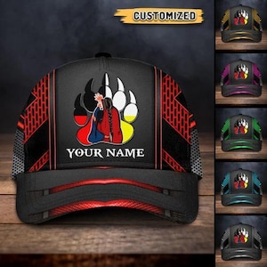 May include: A black baseball cap with a red and black geometric pattern on the sides. The front features a Native American design with the text "YOUR NAME" below it. The word "CUSTOMIZED" is at the top.