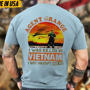 May include: Light blue t-shirt with the text "AGENT ORANGE" and a graphic of a soldier in front of a sunset. The text "I WAS KILLED IN VIETNAM I JUST HAVEN'T DIED YET" is printed below the graphic. The words "MADE IN USA" are printed in the upper left corner.