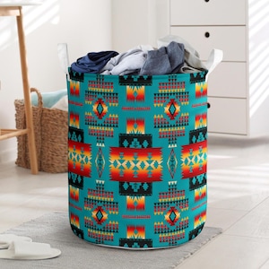 May include: A cylindrical laundry hamper with a turquoise background and a Southwestern geometric pattern in red, yellow, and black. The hamper has white handles and is filled with folded clothes.