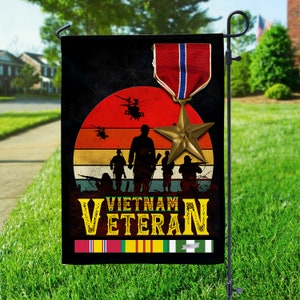 May include: A black garden flag featuring a sunset design with silhouettes of soldiers and helicopters. The flag includes the text "VIETNAM VETERAN" and a military medal with a star.