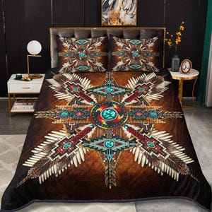 May include: A brown and black quilt set with a Native American design. The quilt features a central starburst pattern with turquoise, red, and white accents. Two matching pillowcases complete the set, creating a cohesive bedroom aesthetic.