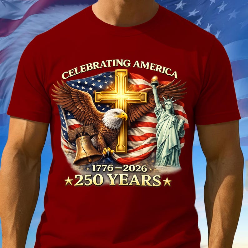 May include: A red t-shirt featuring a patriotic design. The graphic includes a golden cross, an eagle, the Statue of Liberty, and an American flag. Text reads "CELEBRATING AMERICA" and "250 YEARS" with the years 1776-2026.