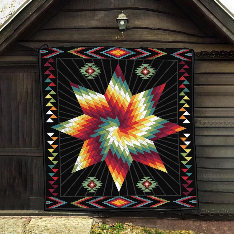 K&ouml;nnte beinhalten: Eine schwarze Steppdecke mit einem gro&szlig;en, farbenfrohen Sternenmuster. Der Stern hat einen Farbverlauf aus Rot, Orange, Gelb und Gr&uuml;n. Die Steppdecke hat einen geometrischen Rand mit Dreiecken und Rauten.