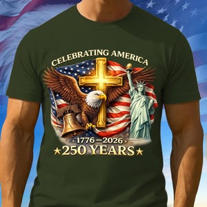 May include: Dark green t-shirt featuring a patriotic design. The graphic includes a golden cross, an American flag, an eagle, the Statue of Liberty, and the text "CELEBRATING AMERICA" and "250 YEARS". The shirt commemorates the years 1776-2026.