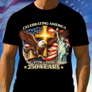 May include: Black t-shirt featuring a patriotic design. The graphic includes an American flag, a golden cross, an eagle, the Statue of Liberty, and the text "CELEBRATING AMERICA 1776-2026 250 YEARS".
