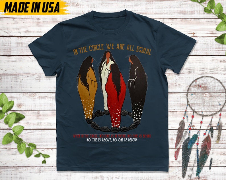 Puede incluir: Camiseta azul marino con el texto "IN THE CIRCLE WE ARE ALL EQUAL". La camiseta presenta una ilustraci&oacute;n de tres figuras en un c&iacute;rculo. Las palabras "NO ONE IS ABOVE, NO ONE IS BELOW" tambi&eacute;n est&aacute;n impresas. Hecho en EE. UU.