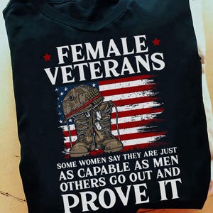 May include: Black t-shirt featuring the text "FEMALE VETERANS" above an American flag design. Below the flag are military boots and a helmet. The shirt also includes the text "SOME WOMEN SAY THEY ARE JUST AS CAPABLE AS MEN OTHERS GO OUT AND PROVE IT."
