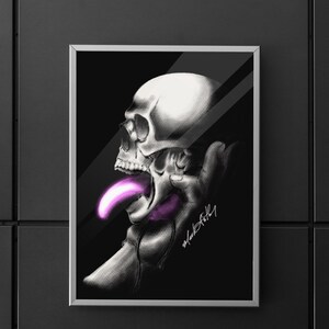 Puede incluir: Obra de arte enmarcada que presenta una ilustración en escala de grises de una calavera con una larga lengua púrpura brillante. La calavera está sostenida por una mano, sobre un fondo negro. La obra tiene una estética moderna y atrevida.