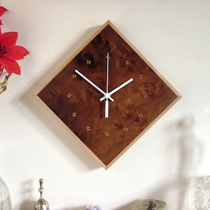 May include: A diamond-shaped wall clock with a brown wood face and white hands. The clock has a light wood frame.