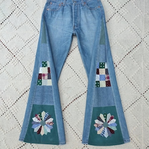 May include: Light blue denim jeans with patchwork and flared legs. The jeans have a button fly and decorative patches of various fabrics. The lower legs feature green corduroy panels with a flower design made of fabric scraps.