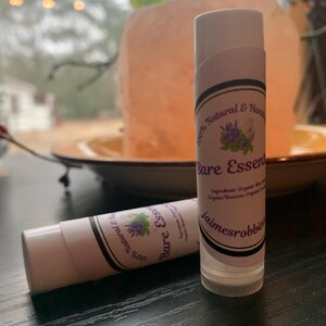 May include: Two white lip balm tubes with black and purple labels. The labels read "100% Natural & Handmade" and "Bare Essentials".