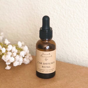 May include: A brown glass bottle with a black dropper top and a label that reads "Sweet Caramel Car Diffuser Refill Cranberry Peppermint Net Wt 1 oz (28 gr)"