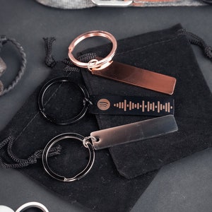 May include: Three silver keyrings with black and rose gold rectangular tags. One tag has a Spotify logo and a barcode. The keyrings are on a black velvet pouch.