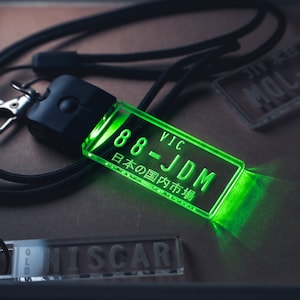 May include: A green acrylic keychain with the text "88 - JDM VIC 日本の国市場" on it. The keychain is attached to a black lanyard.
