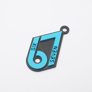 May include: A black and cyan pendant featuring the number 67 with the word SIX embossed on the number 6 and the word SEVEN embossed on the number 7. The pendant has a diamond-like shape with a circular hole at the top for attachment purposes.