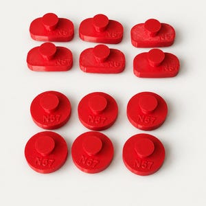 May include: A collection of twelve red plastic components, including six rounded rectangular pieces and six circular pieces. Each component features a raised central knob and the embossed text N57 on the top surface.