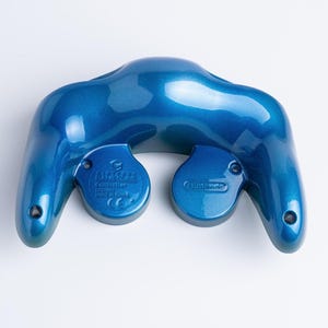 May include: A metallic blue Nintendo GameCube controller back shell featuring a smooth, glossy finish. The moulded plastic casing displays the Nintendo logo and controller text embossed on the rear, with screw holes visible on the two handles.