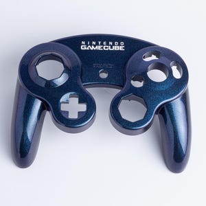 May include: A dark blue, glitter-finish Nintendo GameCube controller front shell replacement. The plastic housing features cutouts for the analogue sticks, buttons, and D-pad, with the Nintendo GameCube logo printed in white at the top centre.
