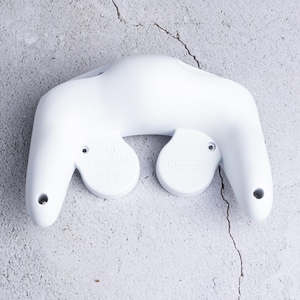 Könnte beinhalten: Rückansicht eines weißen Nintendo GameCube-Controllers. Der Controller hat eine markante Form mit zwei abgerundeten Abschnitten und zwei kreisförmigen Knöpfen. Die Oberfläche ist glatt und das Design minimalistisch.