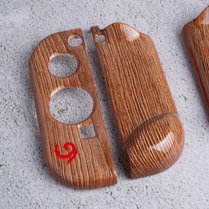 May include: Wooden-textured controller shells with a glossy finish. The shells have a wood grain pattern and a red number 9 is visible on one of the shells. The shells have circular and square cutouts.