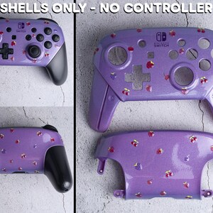 Op de afbeelding: Paarse Nintendo Switch Pro controller shell met een glitterafwerking en een patroon van kleine rode en gele bloemen. De controller heeft zwarte handgrepen en knoppen. De tekst "SHELLS ONLY - NO CONTROLLER" staat bovenaan.