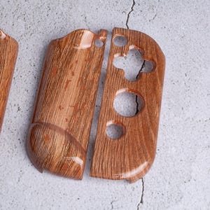 May include: Wooden-textured Switch Joy-Con controller shells. The shells are a warm brown color with a wood grain pattern. The design includes button and joystick cutouts, and a glossy finish.