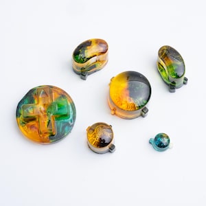 May include: A set of five resin controller buttons featuring a swirling marbled pattern of amber, yellow, and deep green. The collection includes a circular directional pad, two oval buttons, one large round button, and two smaller round buttons.