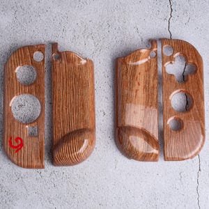 May include: Set of two wooden-look controller shells for a gaming console. The shells are a warm brown color with a wood grain pattern and glossy finish. Each shell has cutouts for buttons and controls.