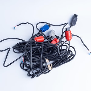 Könnte beinhalten: Ein verwirrtes Bündel schwarzer Elektrokabel mit verschiedenen farbigen Kunststoffsteckern, darunter rote, blaue und graue Komponenten. Die Kabel sind mit zwei kleinen beigen Gummibändern zusammengehalten und einige Enden liegen frei.