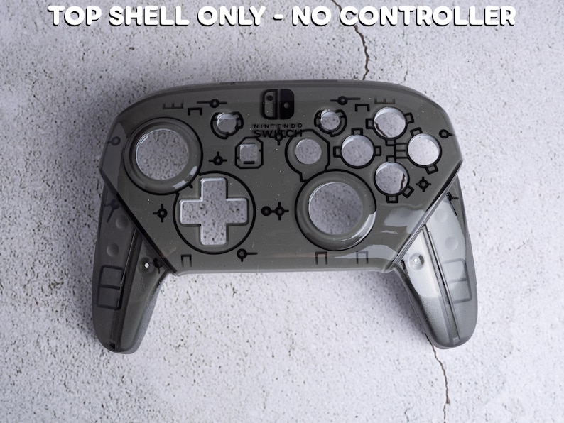 Op de afbeelding: Een grijze Nintendo Switch Pro Controller bovenste schaal. De controller heeft een transparant ontwerp met zichtbare knoppen en een D-pad. De tekst "TOP SHELL ONLY - NO CONTROLLER" staat bovenaan.