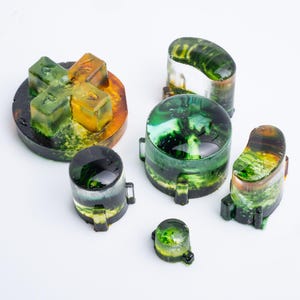 May include: A set of five custom resin controller buttons featuring a translucent finish with swirling green, yellow, and black pigments. The collection includes a directional pad, two circular buttons, and two curved action buttons with glossy surfaces.