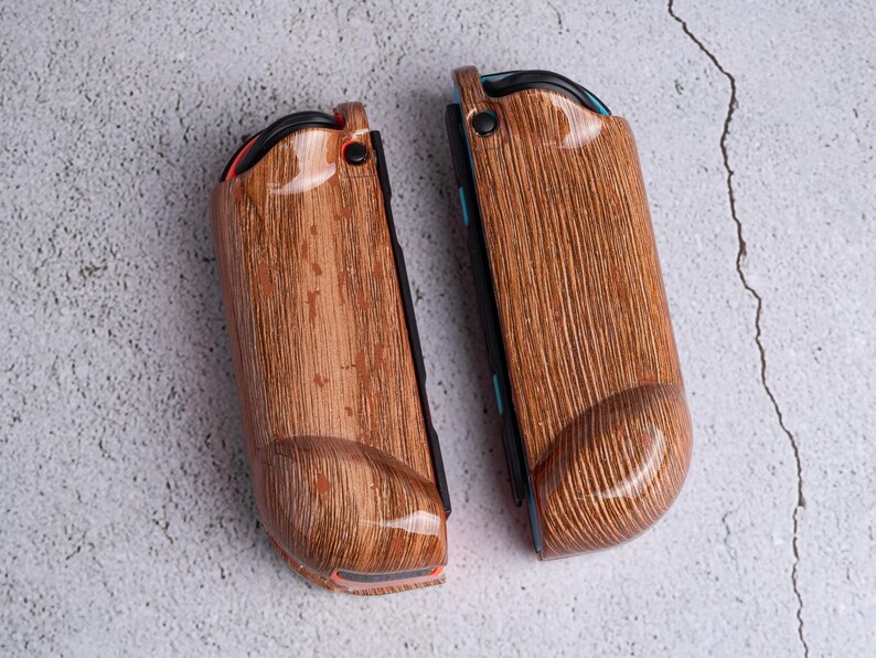 May include: Two wooden-textured Joy-Con controllers for a gaming console. The controllers have a brown wood grain pattern with a glossy finish. The design includes black, red, and blue accents. The controllers are designed to enhance the gaming experience.