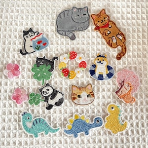 May include: A collection of iron-on patches featuring various cute animal designs, including cats, pandas, dinosaurs, and a flower wreath. The patches are perfect for adding a touch of whimsy to clothing, bags, or other fabric items.
