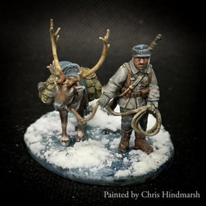 Könnte beinhalten: Eine Miniaturfigur eines Soldaten mit einem blauen Hut und einer braunen Uniform, der ein Seil hält und neben einem Rentier mit Sattel und Packung auf dem Rücken steht. Die Szene spielt auf einer schneebedeckten Basis.