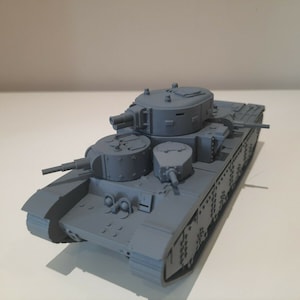 May include: A grey model tank with multiple turrets and a rectangular body. The tank has detailed features, including gun barrels and track treads. The model is set against a plain background.