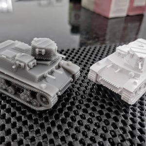 May include: Two 3D printed toy tanks, one grey and one white, on a black and white grid surface.