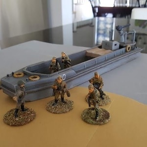 Peut inclure: Un modèle gris de débarquement avec un équipage de soldats miniatures peints. Les soldats portent des uniformes de camouflage et tiennent des fusils. Le débarquement est posé sur une surface brune.
