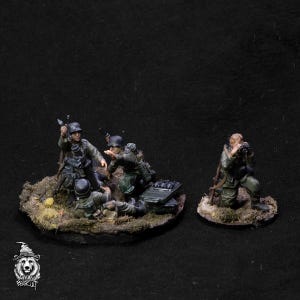 May include: Four painted miniature figures of German soldiers in World War II era uniforms. Three soldiers are operating a mortar, while the fourth soldier is standing with a rifle. The figures are on a circular base with a green and brown textured surface.