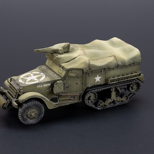 Op de afbeelding: Een groen militair halfrupsvoertuig met een canvashoes, een witte ster aan de zijkant en de tekst "U.S.A. 3005737".