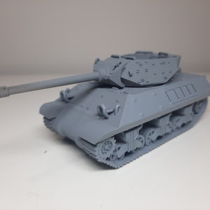 以下が含まれることがあります： 長い砲身と詳細な砲塔を持つ灰色のプラスチック製の戦車のモデル。戦車は履帯式で、白い表面の上に置かれています。