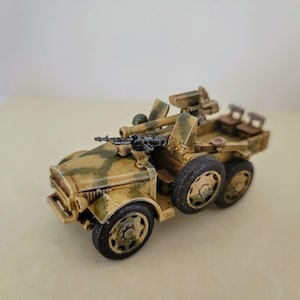 Op de afbeelding: Een gedetailleerd model van een militair voertuig, geschilderd in een woestijncamouflagepatroon. Het voertuig heeft een groot kanon gemonteerd aan de achterkant en een kleiner machinegeweer aan de voorkant. Het model is gemaakt van plastic en is ongeveer 1/35 schaal.