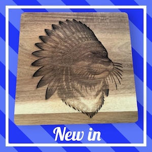 May include: Wooden cutting board with a detailed engraved image of an animal wearing a Native American headdress. The board has a natural wood grain finish and the text "New in" is displayed at the bottom.