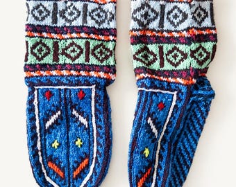 Puede incluir: Un par de calcetines de lana tejidos a mano con una base azul vibrante y complejos patrones geométricos en blanco, negro, naranja, verde y amarillo. Los puños muestran bandas horizontales de rombos y los pies un motivo central tipo escudo.