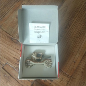 Puede incluir: Una pequeña escultura en miniatura de gres marrón de un coche antiguo en una caja blanca. La caja tiene una etiqueta que dice "Stoneware Miniature Sculptures by Trenmar Potteries."