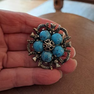 Könnte beinhalten: Eine silberne Brosche mit einem Design aus sechs türkisblauen Steinen, umgeben von silbernen Distelmotiven.
