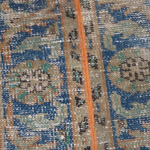 May include: Close-up of a blue and brown patterned rug with a detailed design. The rug has a fringe border and a subtle orange stripe running down the center.