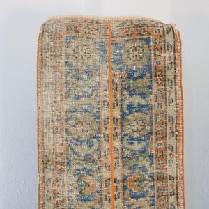 May include: A vintage rug with a faded orange, blue, and green floral pattern. The rug has a worn, distressed look and is perfect for adding a touch of bohemian style to your home.