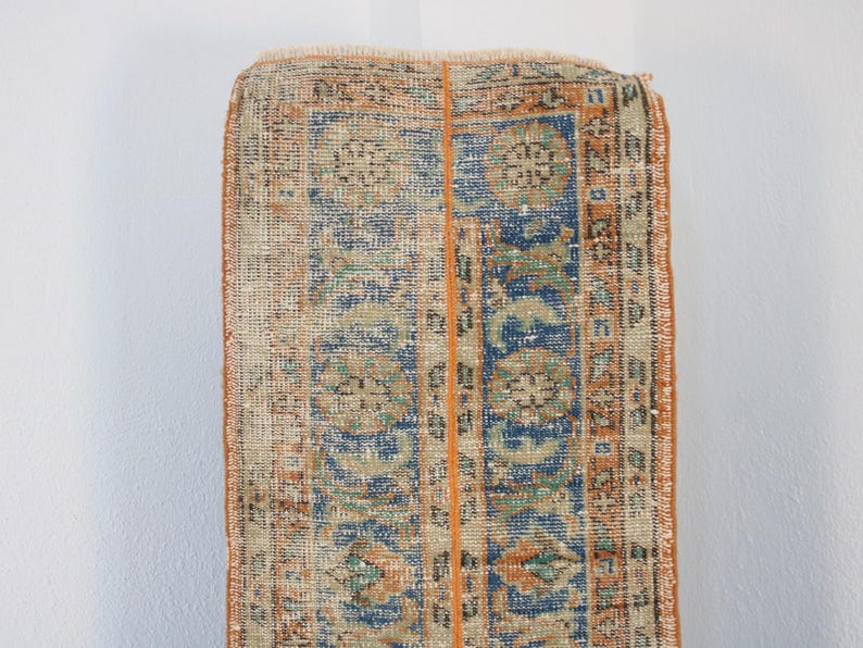 May include: A vintage rug with a faded orange, blue, and green floral pattern. The rug has a worn, distressed look and is perfect for adding a touch of bohemian style to your home.